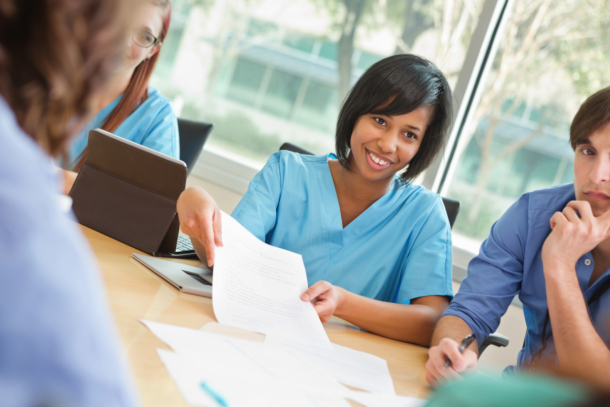 Female Nurse handing paper to a colleage around a busy table