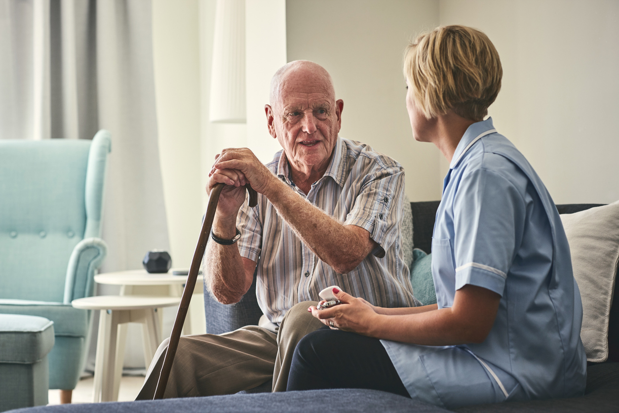 Female Carer with Elderly man who has a walking stick sitting down