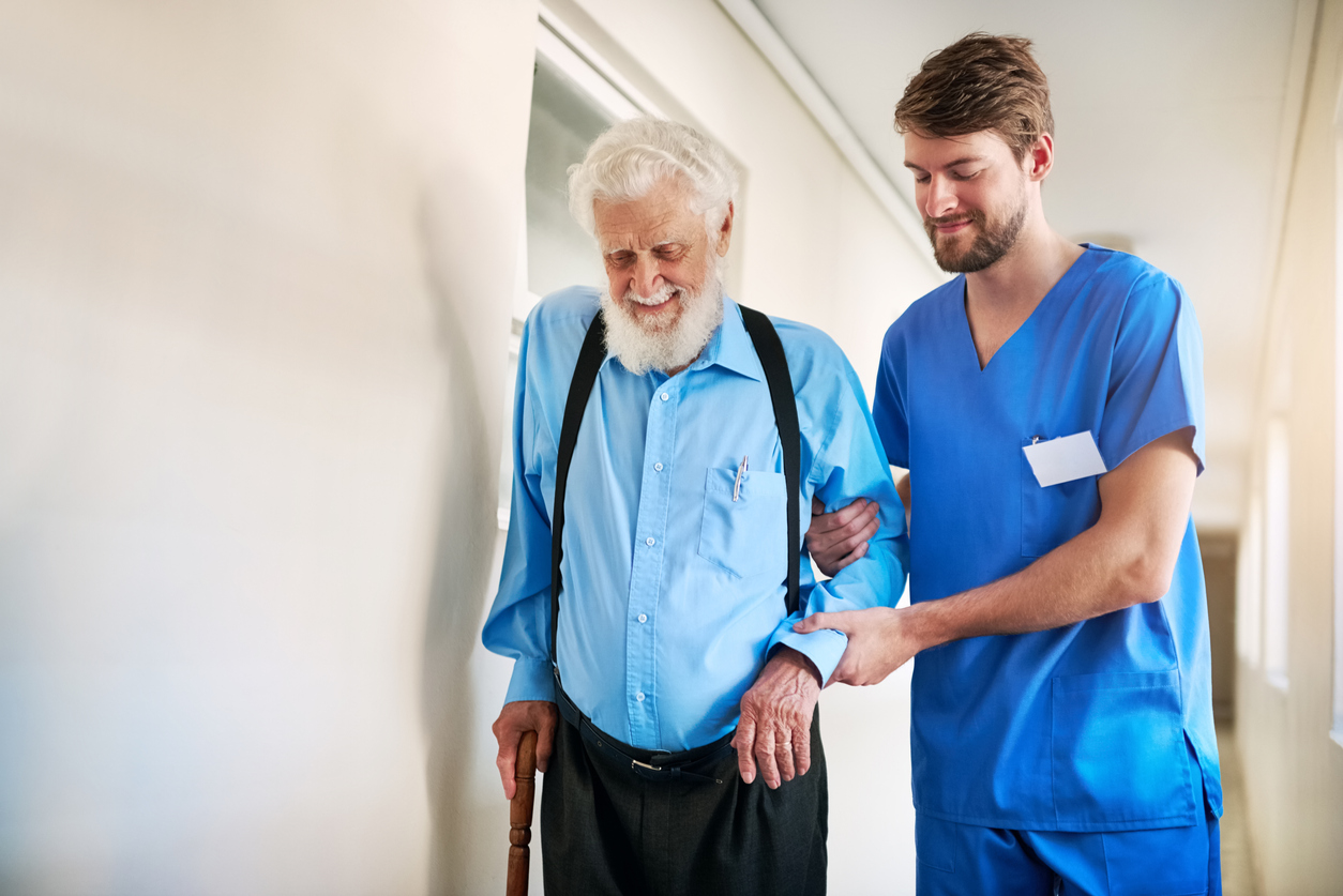 Male Carer with Elderly man with a walking stick walking down a coridor
