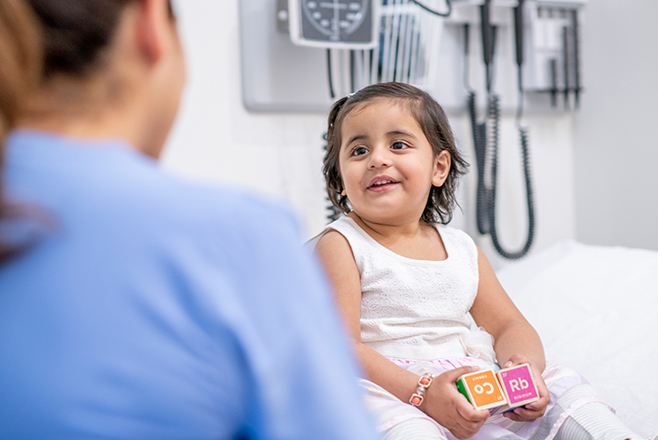 A child sitting on a hospital bed talking to a nurse