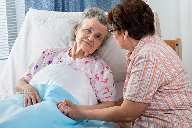 A caregiver holding the hand of an elderly woman in bed