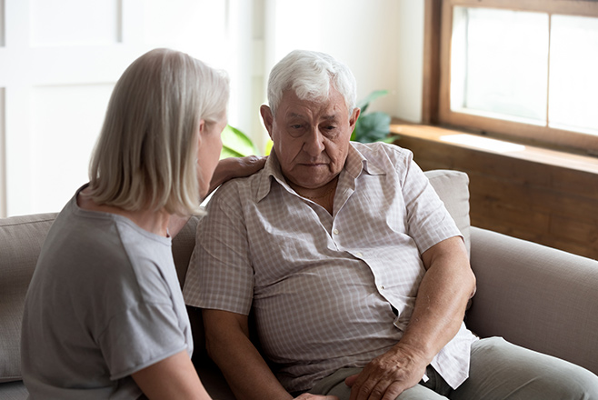 A caregiver talking to an elderly man on a couch