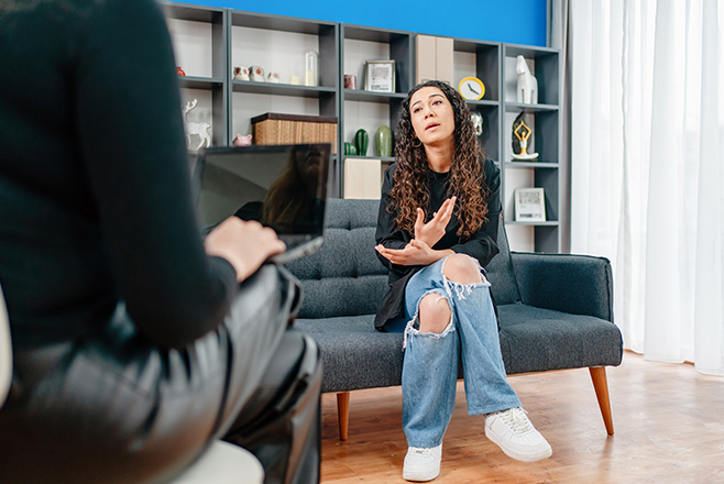 A woman with a laptop talking to a woman on a couch