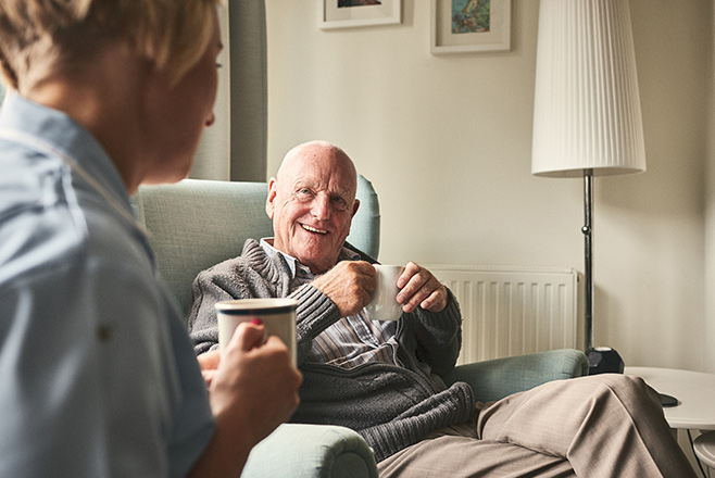 Nurse with a man who is smiling and having a cup of tea