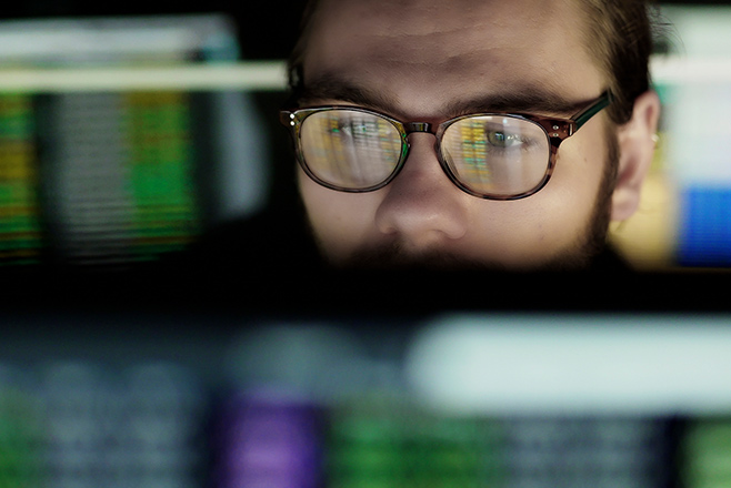 A man wearing glasses reflecting a computer screen