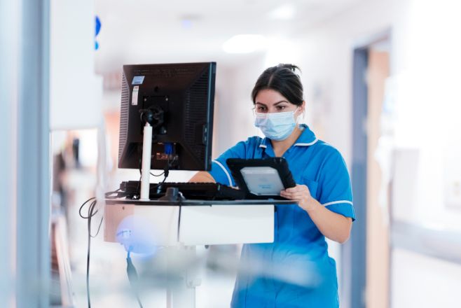 A female nurse using a digital tablet and standing by a monitor
