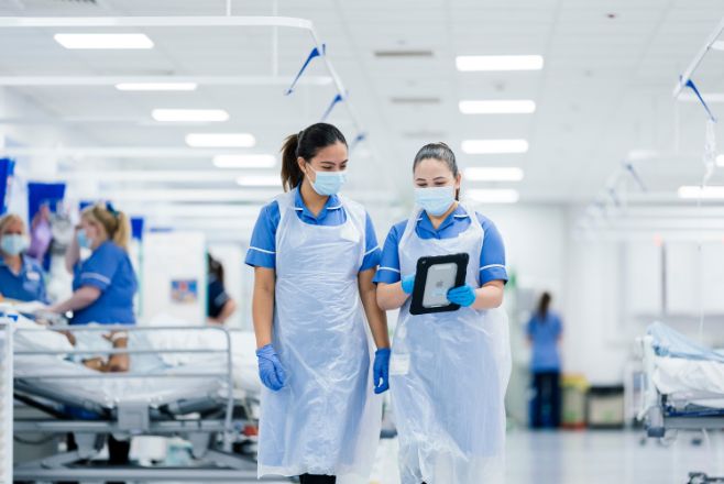 Two female nurses walking along and looking at a digital tablet
