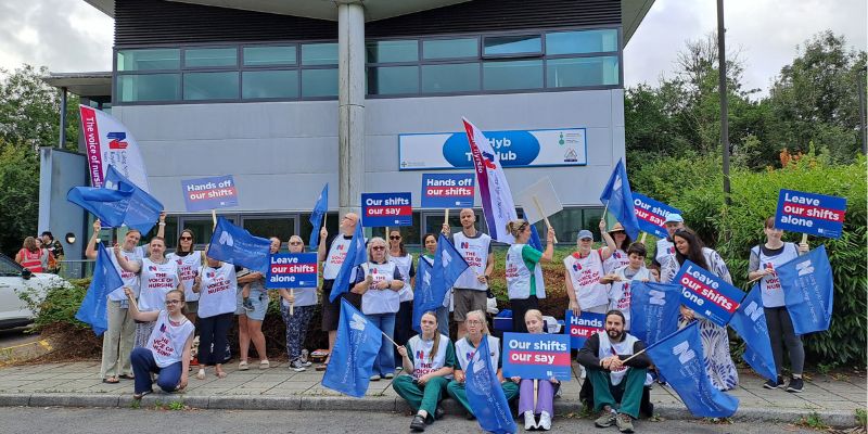 RCN members and staff stand and wave RCN branded flags outside the Cwm Taf Morgannwg University Health Board meeting