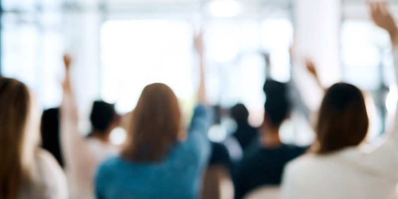Rearview shot of a group of businesspeople raising their hands to ask questions during a conference