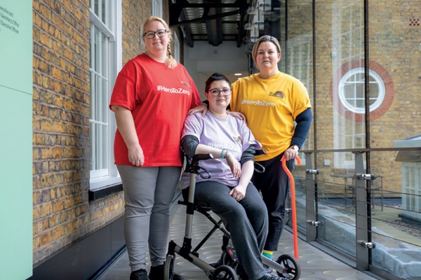 A group of three women - one in a wheelchair, one standing with a cane and one standing