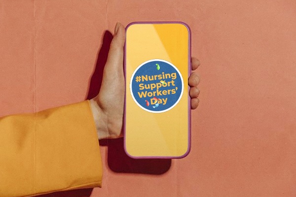 A hand holding a phone with 'Nursing Support Workers Day' on the screen