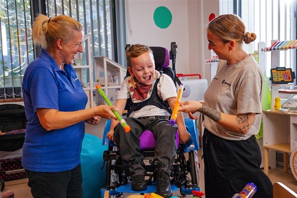Two nursing support workers smiling and playing with a boy in a wheelchair