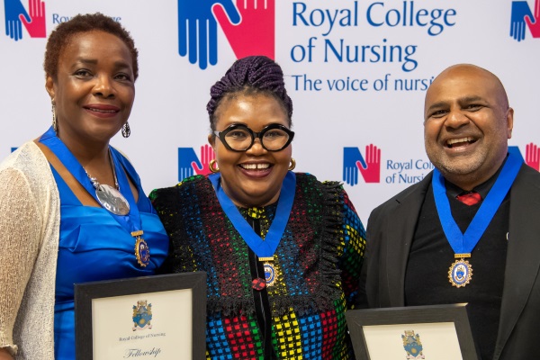 Three smiling people wearing medals and holding certificates in front of a Royal College of Nursing backdrop
