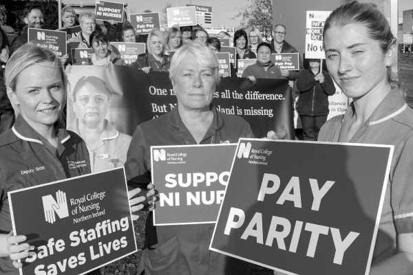 Nursing staff holding a demonstration with signs saying 'pay parity' and 'safe staffing saves lives'