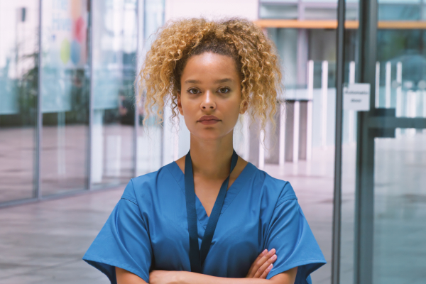 Female nurse wearing scrubs standing in a hospital with her arms crossed and looking serious 