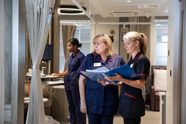 Two members of nursing staff reading through a folder with another member of nursing staff using a computer in the background
