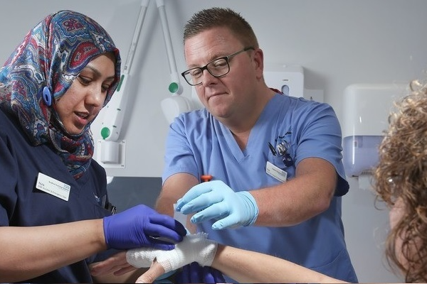 Nursing support worker assisting a nurse colleague with a procedure.