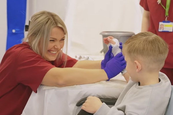 A smiling nursing support worker treating a child with his arm in a cast