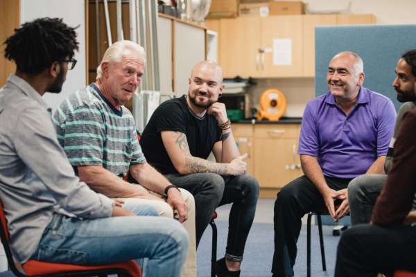 Image of five men sitting on chairs in a support group setting
