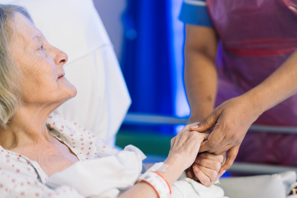 Picture of older woman in bed holding hands with a nurse