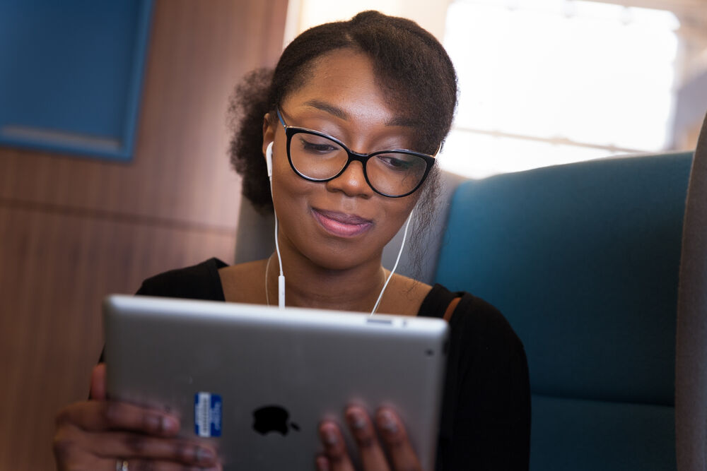 A person wearing glasses and earphones looks at a tablet while seated on a train or bus.