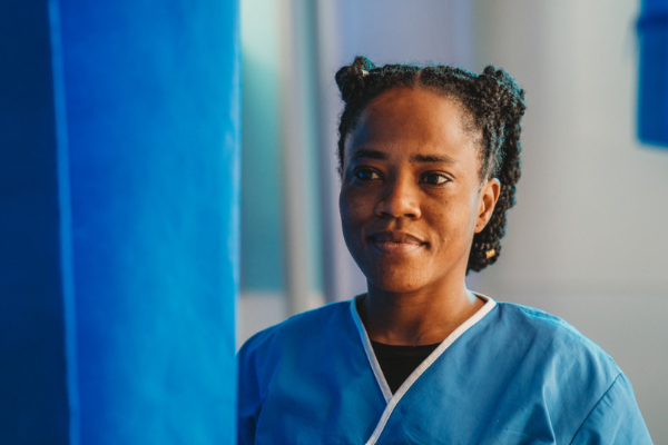 A portrait of a female nurse in blue scrubs looking thoughtfully off-camera.