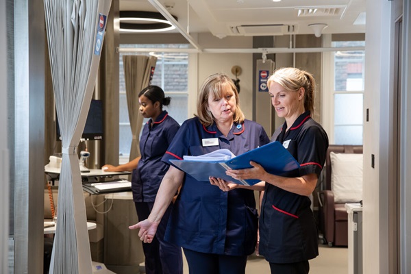 Two members of nursing staff reading a document in a folder while another works on a computer
