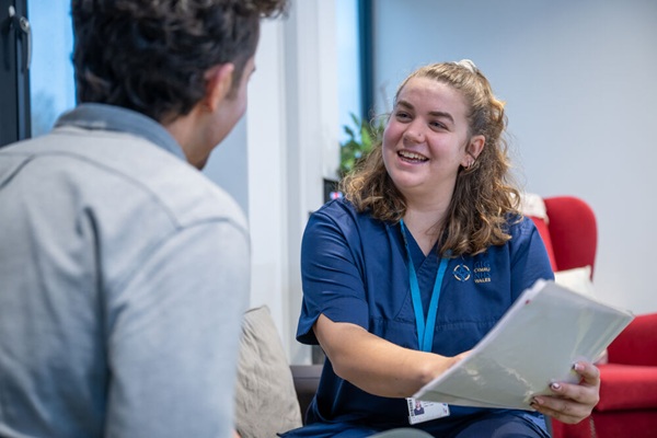 A smiling nurse holding a folder and speaking to a patient