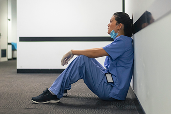A nurse sitting against the wall in a hallway looking tired
