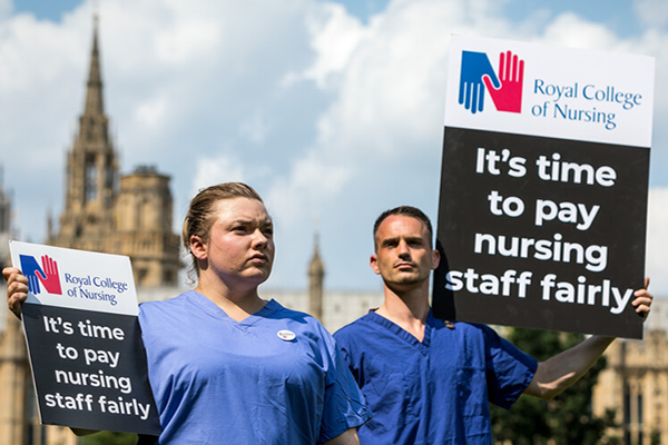 Nurses standing together with signs that say "It's time to pay nursing staff fairly.