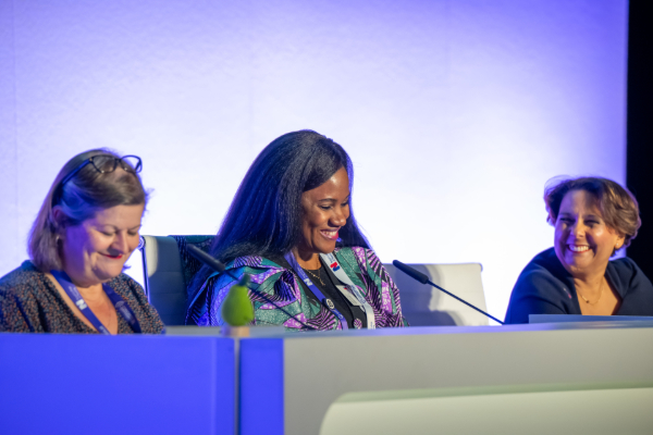 Three smiling women seated at a panel table with microphones during a conference discussion.