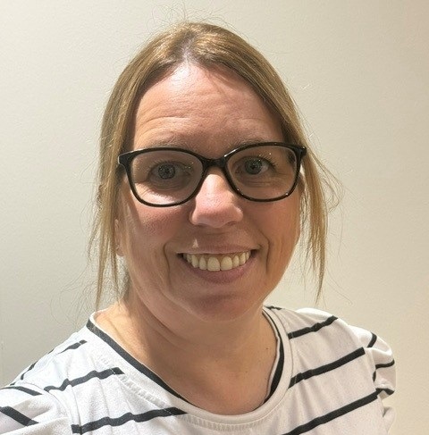 a headshot of Hilary Nelson, a woman with blonde hair, glasses and a striped t-shirt