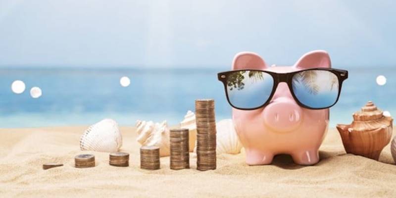 Piggy bank in shades on the beach with piles of coins 800x400