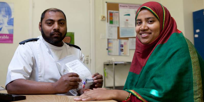 Male Asian nurse with Asian woman smiling Male Asian nurse with beard looking serious sitting with an Asian woman wearing a maroon headscarf and green dress with gold trim, smiling