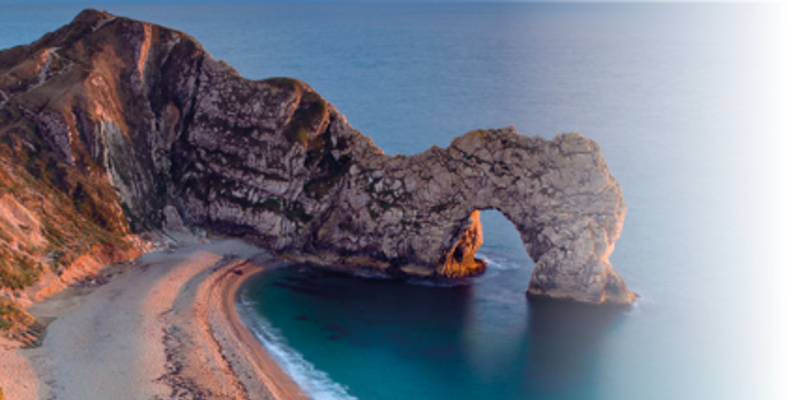 Dorset Lulworth Cove - sandy yellow beach and cliffs with rock formation on the left with an archway and tunnel surrounded by blue sea