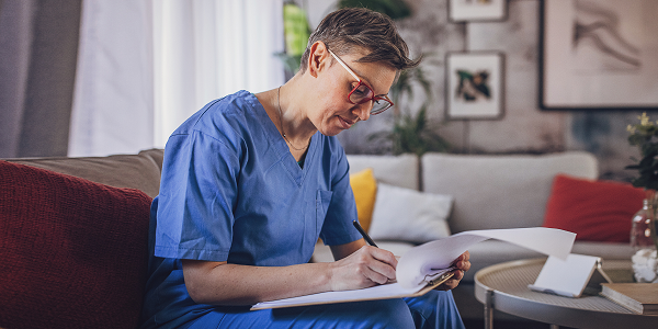 Older female nurse in scrubs sat on the sofa doing paperwork