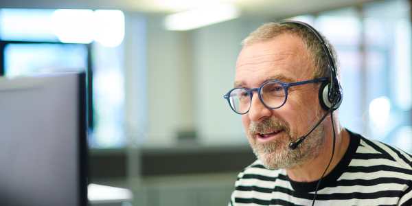 Male adviser at computer in an office, talking on a headset