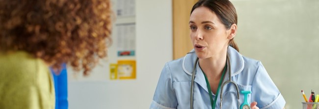 A healthcare professional with a stethoscope speaks to a patient, who is seen from behind, during a consultation.