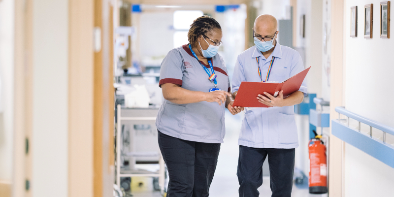 Two nurses looking at a folder in a corridor