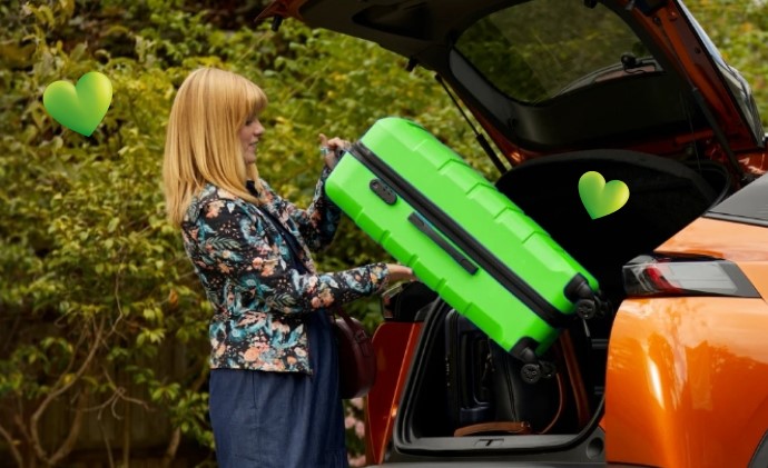 LV travel insurance woman putting large green suitcase into car boot