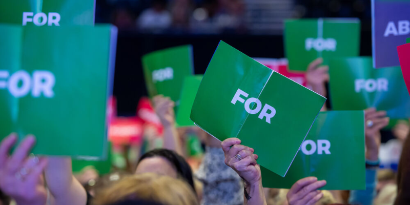 Hands hold up signs to vote "For" or "Against", or to "Abstain" from the vote.