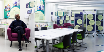 Image showing the temporary exhibition space and a person sitting in a chair listening to an audio installation.