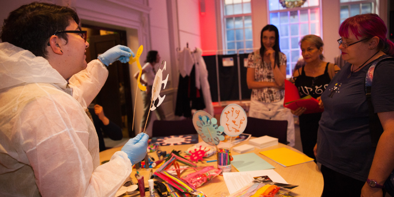 photo of art crafts around a table with people looking at paper bugs