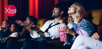 a man and a woman at the cinema, smiling at the screen and holding popcorn. there is an rcn xtra logo in the top left-hand corner