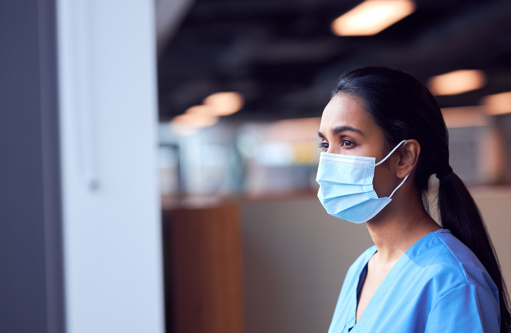 Masked nurse gazing out of the window looking pensive