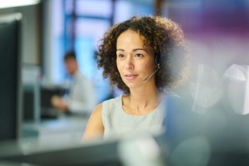 A woman with a headset taking a telephone call at a computer screen.