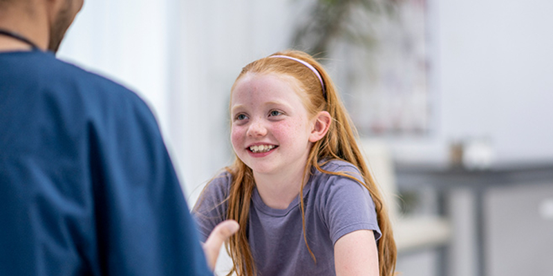 A young girl smiling, talking to a doctor