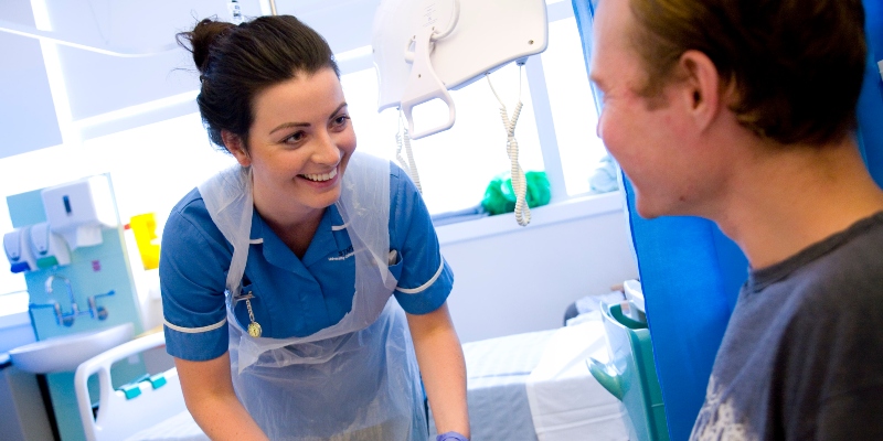 NHS nurse smiles at patient in hospital bed