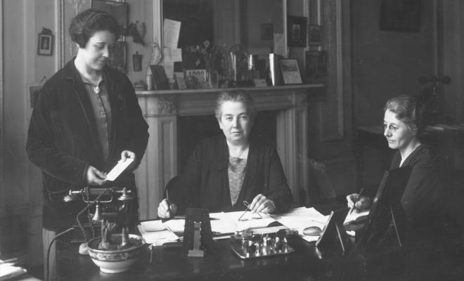 Gertrude Cowlin pictured at a desk with two colleagues at her side.