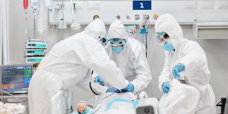 Health care staff in full PPE surround a patient's bed